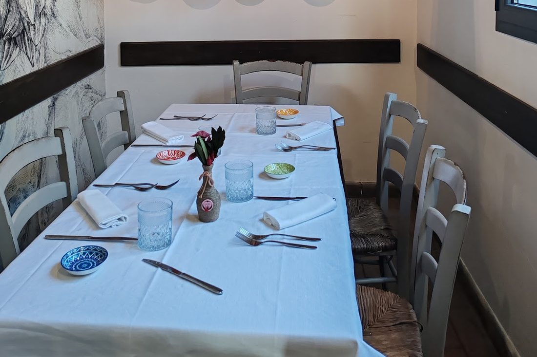 La sala di Casa SaPò: tavola apparecchiata con tovaglia bianca, ceramiche dipinte e murale a carboncino
